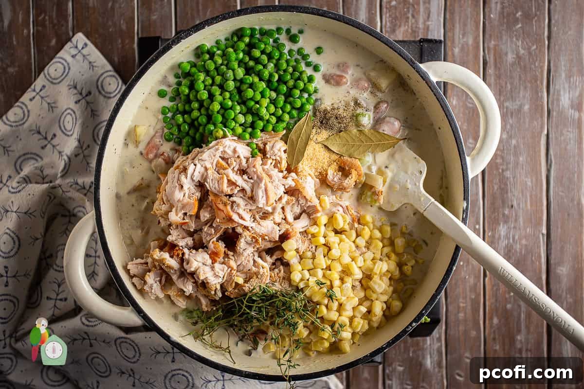 Cooked turkey and frozen vegetables being stirred into the thick, creamy pot pie filling in a large pot.