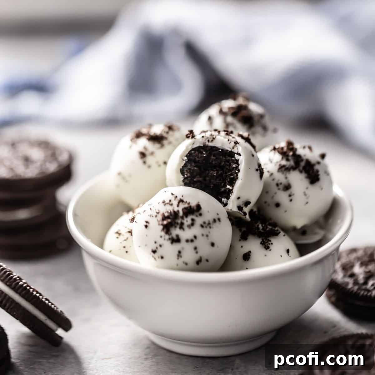An inviting overhead view of delectable Oreo balls presented in a pristine white bowl, glistening with a white chocolate coating and sprinkled with finely crushed Oreo crumbs.