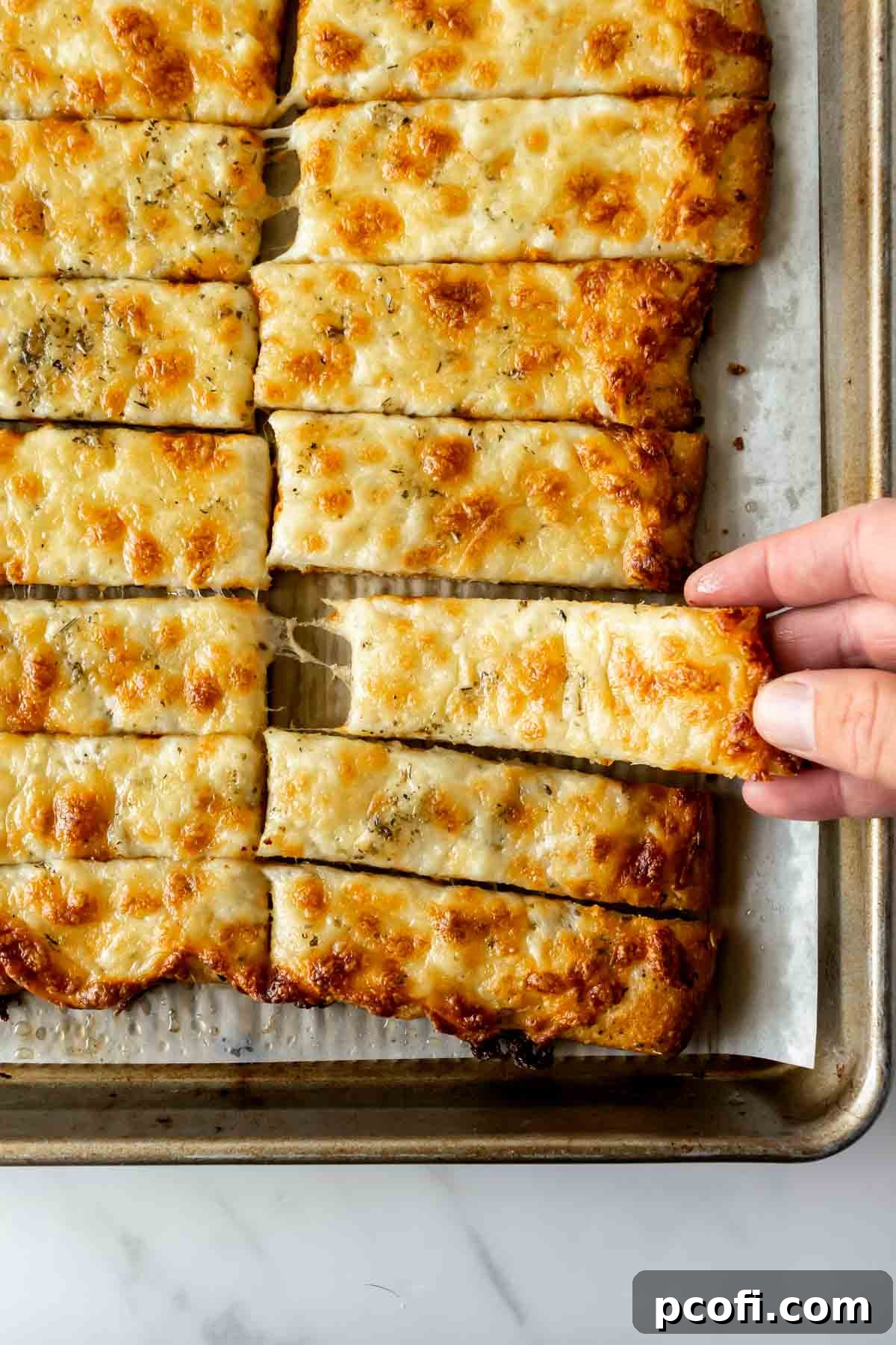 Golden brown strips of cheesy breadsticks on a baking sheet, fresh from the oven and ready to serve.