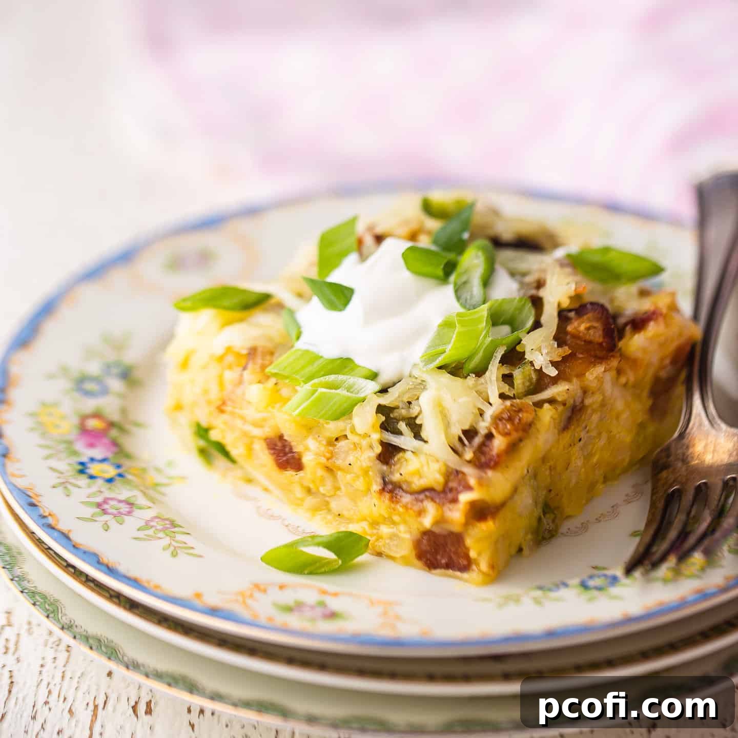 A hearty slice of breakfast casserole artfully arranged on a vintage plate, with a charming pink checked cloth in the background.