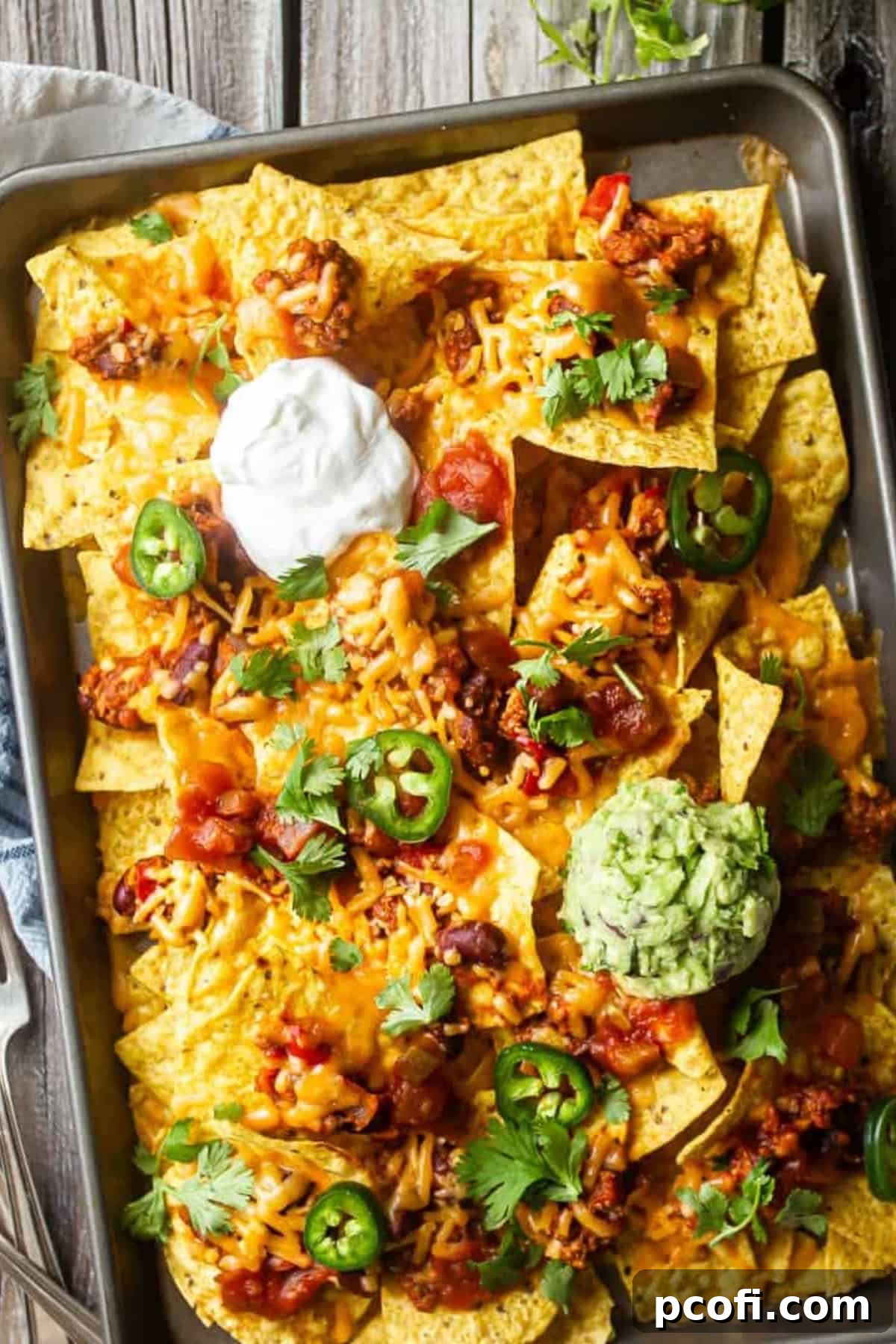 A generous platter of homemade nachos on a sheet pan, beautifully topped with sour cream and fresh guacamole.