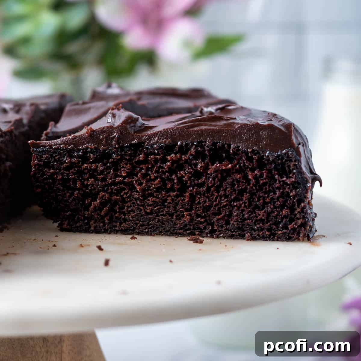 A decadent slice of chocolate fudge cake, glistening with rich frosting, presented elegantly on a cake stand.