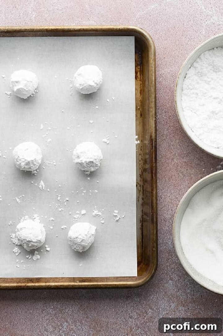 Rolling dough into balls and coating in powdered sugar.