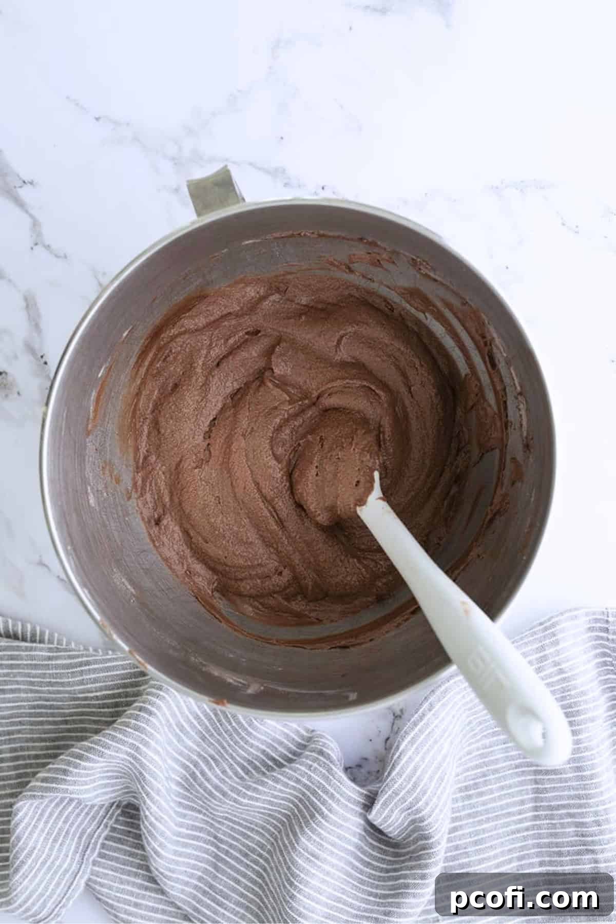 Smooth chocolate cupcake batter in a mixing bowl, being scraped down with a white spatula.