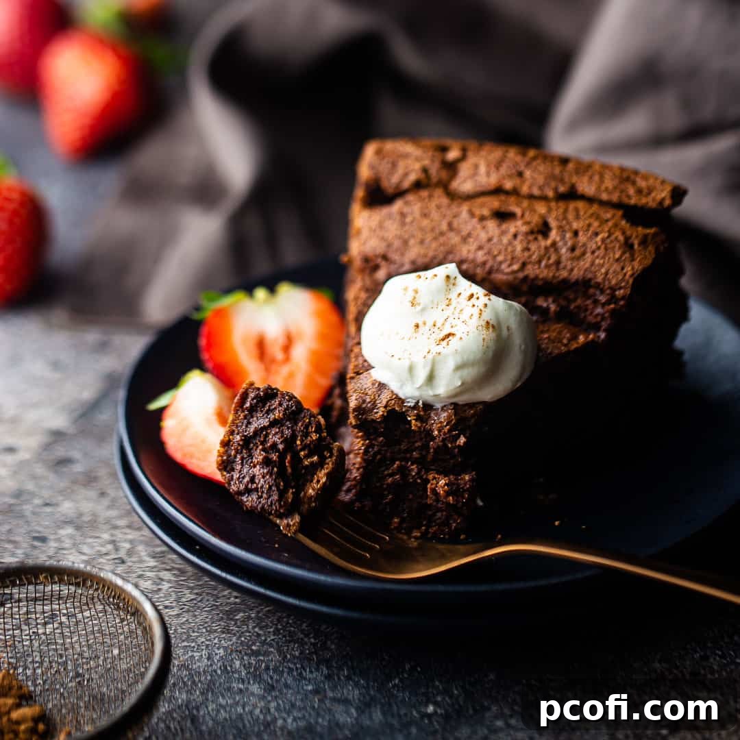 Slice of flourless chocolate cake on a dark blue plate with a rose gold fork.