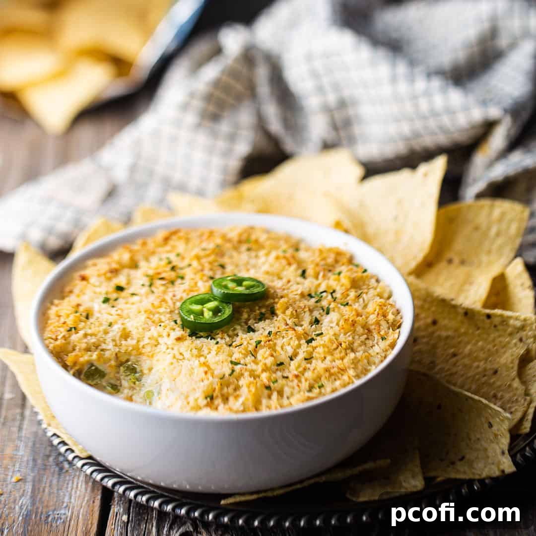 A creamy Jalapeno Popper Dip served in a white ceramic bowl, garnished with two slices of fresh jalapeño pepper.