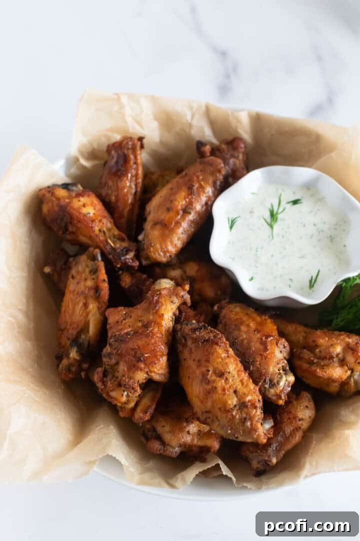 A bowl of golden crispy baked chicken wings, accompanied by a creamy ranch dressing for dipping.