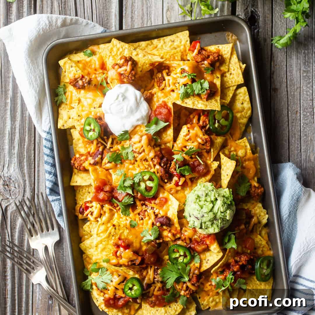 A colorful sheet pan piled high with loaded chicken nachos, garnished with fresh cilantro and jalapeños.