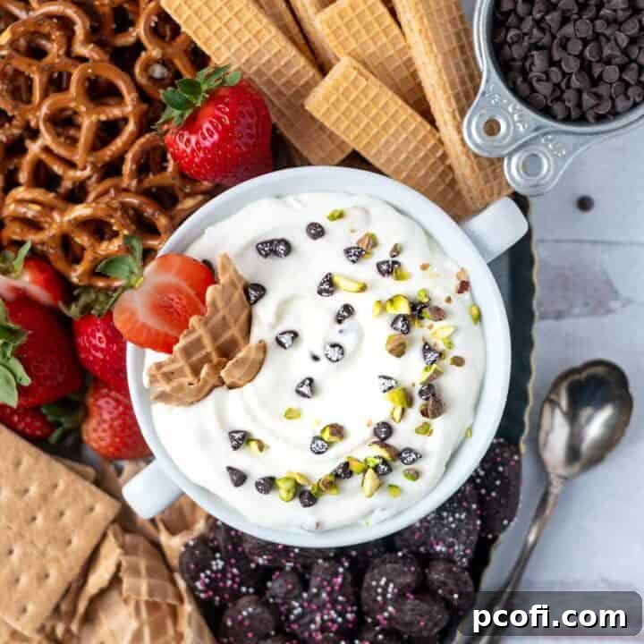 overhead look at cannoli dip with pistachios and chocolate chips on top. Surrounded by pretzels, strawberries and cookies.