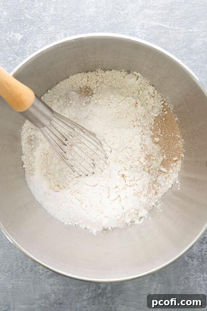 Whisking together dry ingredients: sugar, salt, yeast, and flours in a stand mixer bowl.
