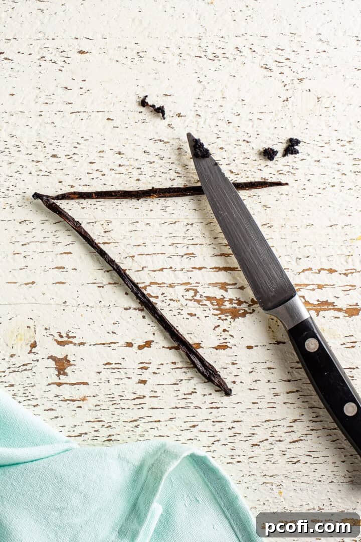 Vanilla bean being split and scraped into milk in a pot.