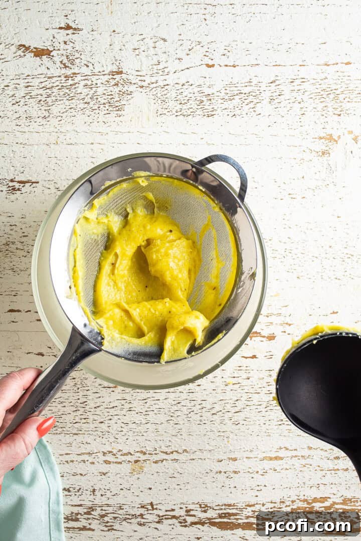 Pastry cream being strained through a fine-mesh sieve into a bowl.