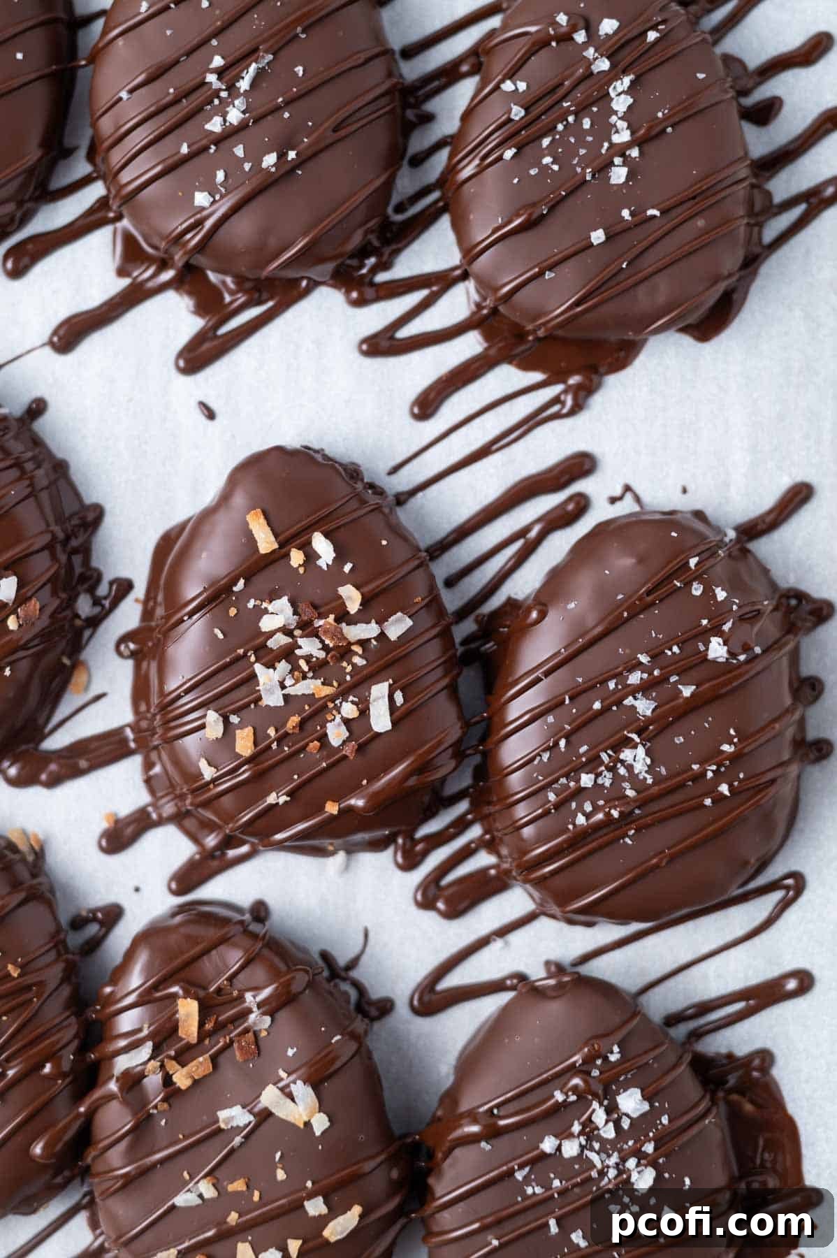 chocolate dipped and drizzled homemade candy on a parchment lined baking pan with coconut and sea salt garnish