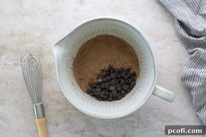 A large bowl containing dry ingredients for chocolate muffins: flour, cocoa powder, baking powder, baking soda, salt, and chocolate chips.