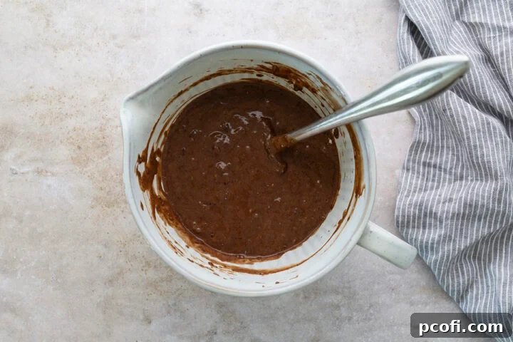 The combined wet and dry ingredients for chocolate muffins, showing a barely mixed batter with a few lumps, in a large mixing bowl.