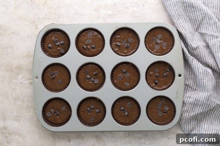 Muffin batter divided evenly into a 12-cup muffin tin, with extra chocolate chips sprinkled on top of each.