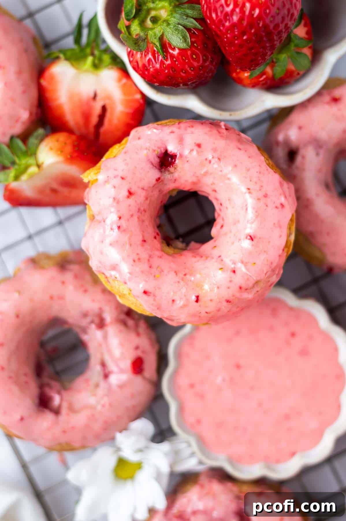 glazed strawberry donut on a cooling rack with a bowl of glaze and fresh strawberries