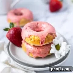 stack of baked strawberry donuts on a plate with strawberries and fresh flowers
