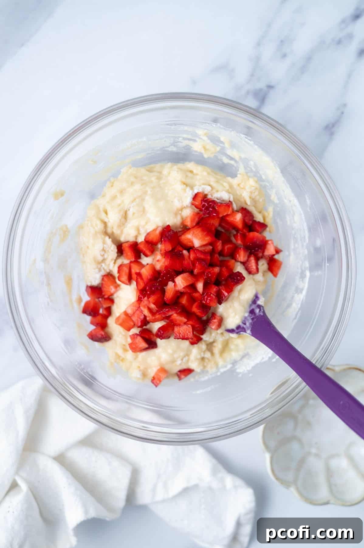 fresh strawberries added to donut batter in a bowl with a spatula