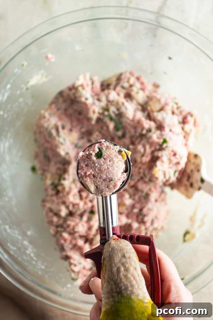 A hand using a 1-tablespoon trigger scoop to portion out the meatball mixture into small, uniform balls.