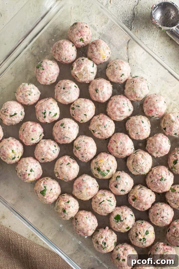 Numerous uncooked mini meatballs arranged neatly in a glass baking dish, ready for baking.