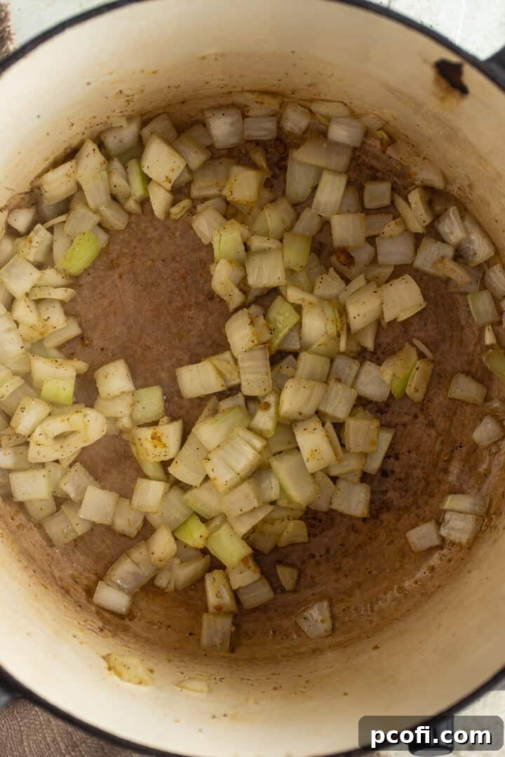 Finely chopped onion being sautéed in olive oil with salt, pepper, and garlic powder in a large pot on the stovetop.