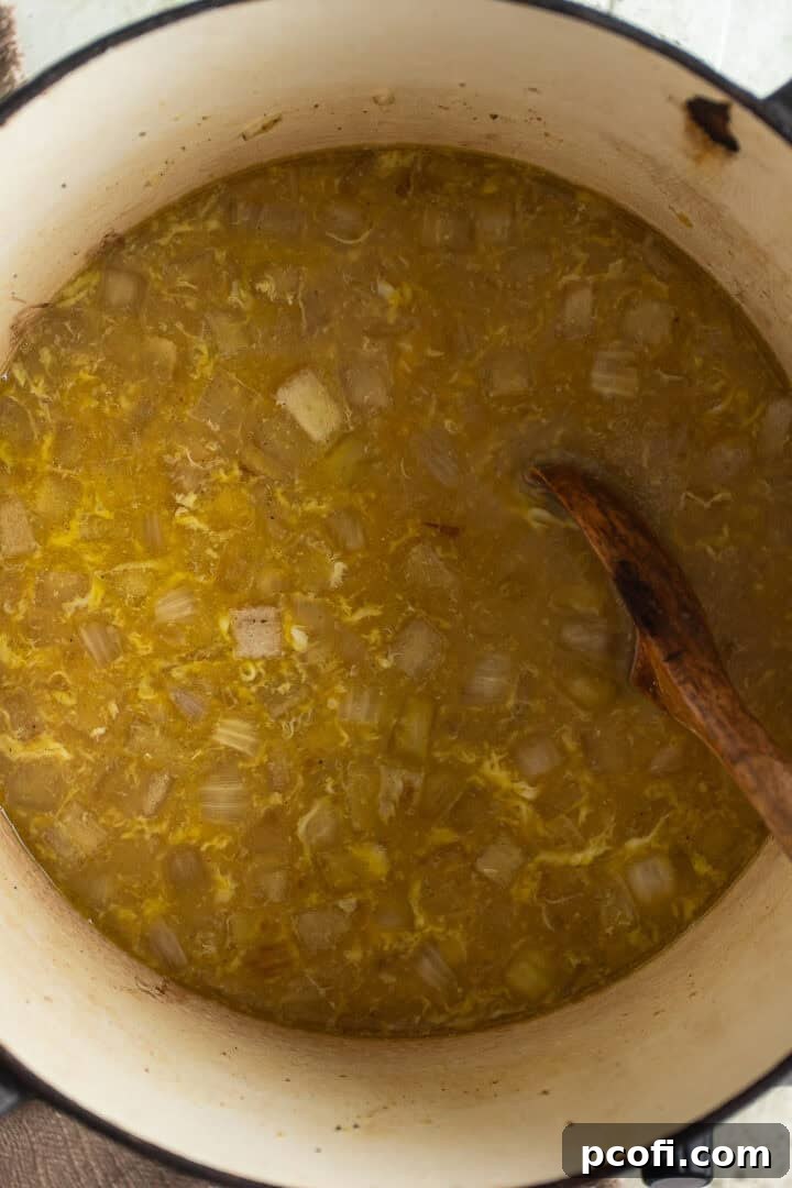 Chicken stock being poured into a pot with sautéed onions, followed by beaten eggs being gently stirred into the simmering liquid.