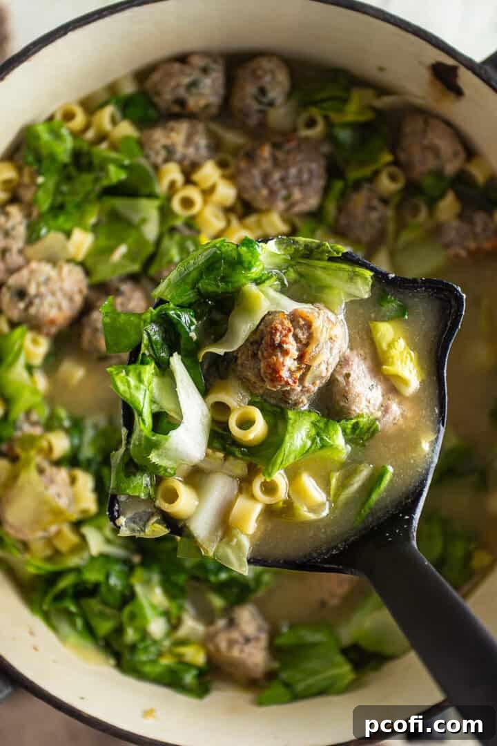 Cooked mini meatballs, chopped escarole, and cooked pastina pasta being added to the simmering chicken broth in a large pot.