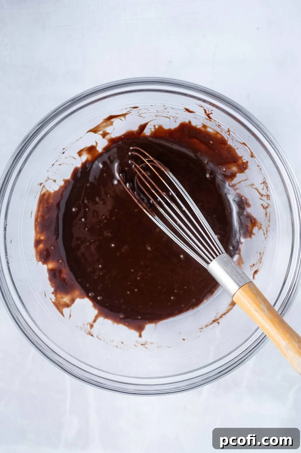 Butter, cocoa powder, egg, sugar, and salt are whisked together in a glass bowl over a double boiler, showing the base mixture thickening.