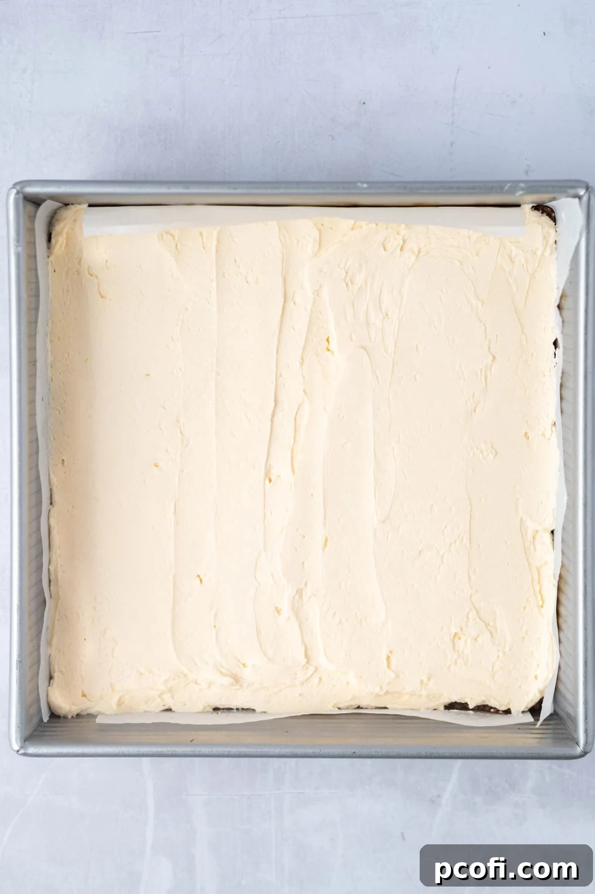 The smooth custard powder filling is evenly spread over the chilled chocolate coconut base in a parchment-lined baking pan.