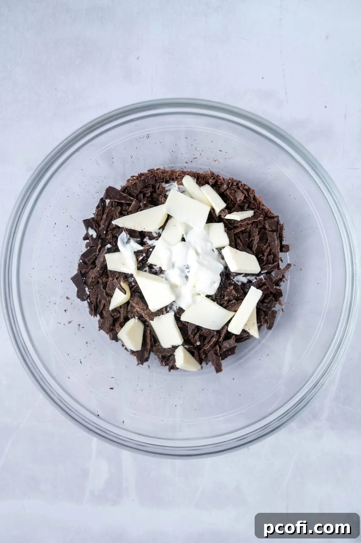Chopped semi-sweet chocolate, butter, and heavy cream are combined in a glass mixing bowl, ready to be melted for the ganache topping.