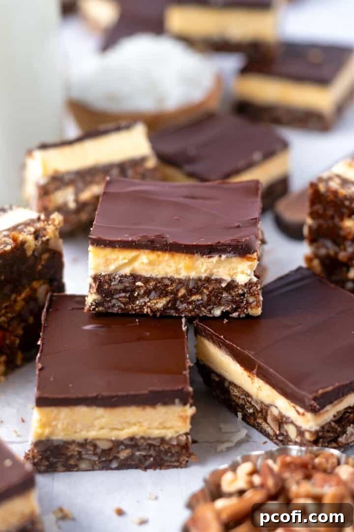 A pile of perfectly cut Nanaimo bars, with bowls of coconut and pecans in the background, highlighting the ingredients.