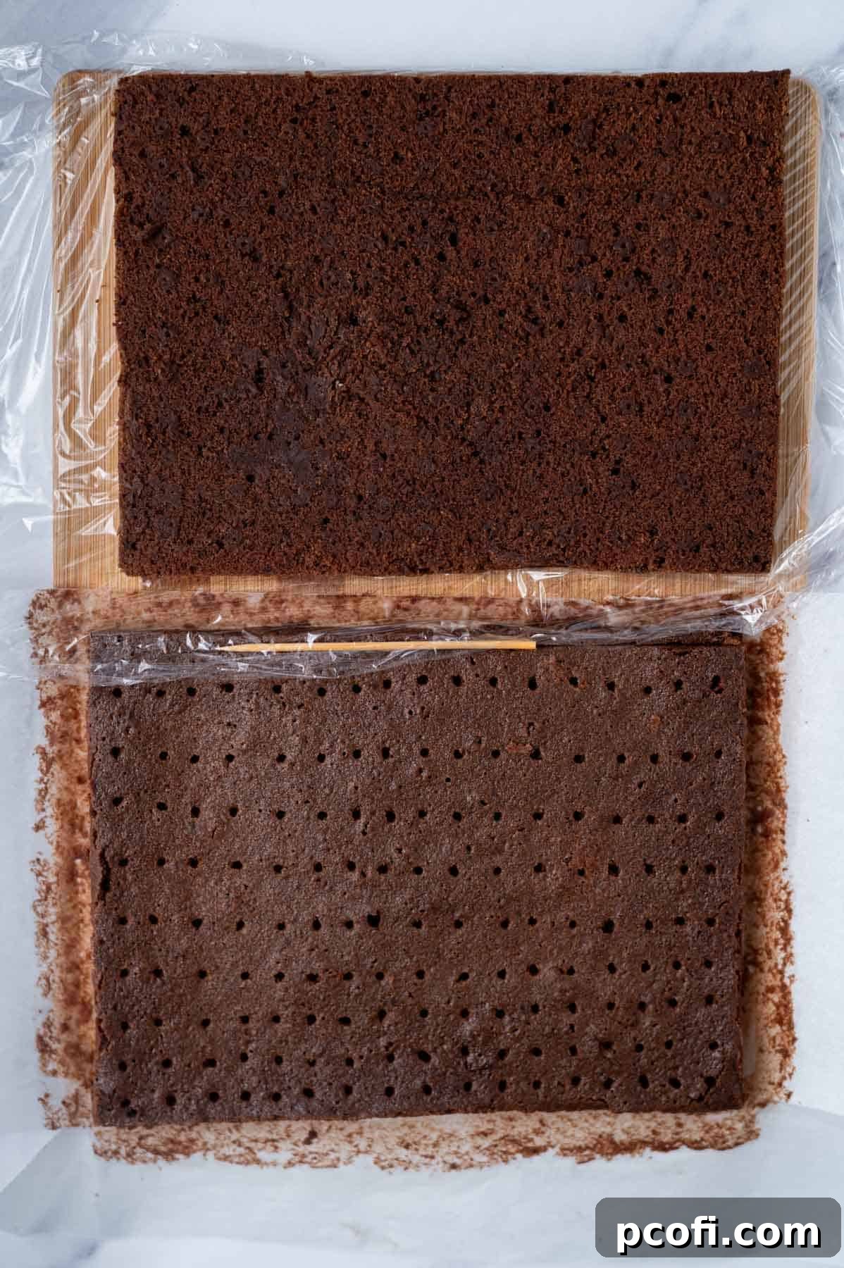 Step 5: Two halves of the cooled and lightly frozen brownie cookie layer on a cutting board, with one layer showing small holes poked into its surface using a bamboo skewer.