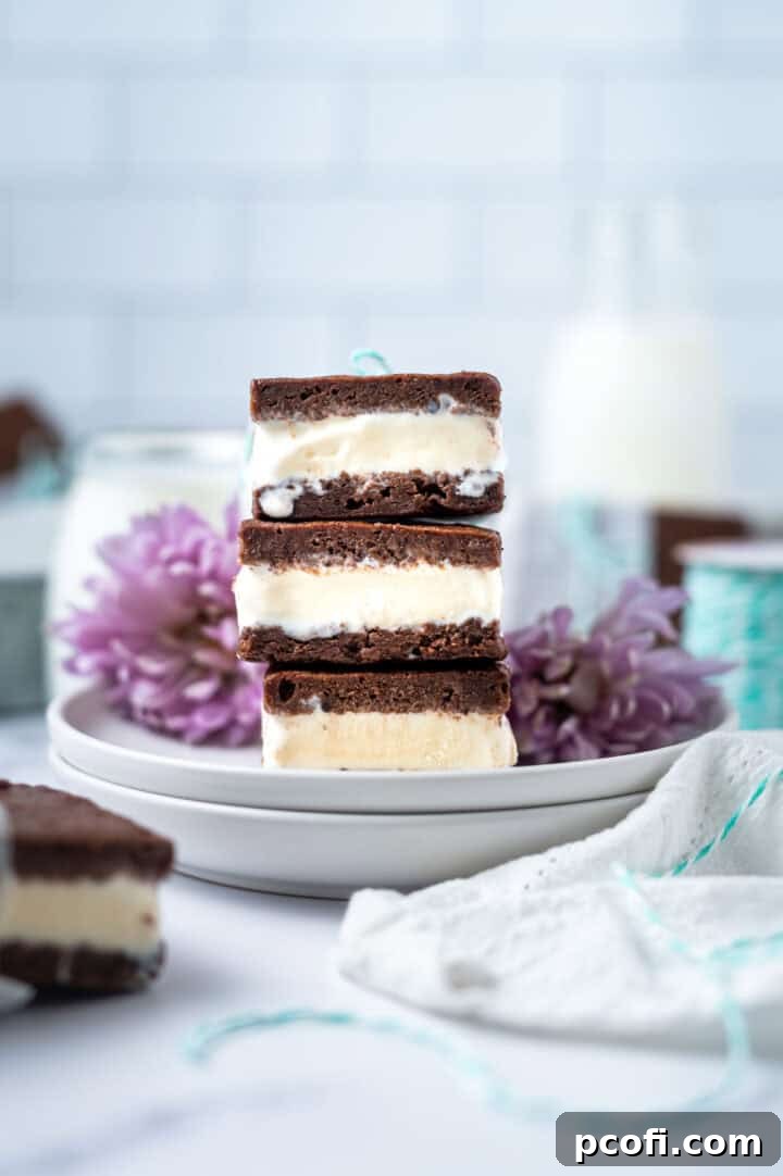 A charming stack of freshly made ice cream sandwiches presented on a white plate, with delicate flowers and a glass of milk visible in the soft-focus background, creating a cozy and inviting dessert scene.
