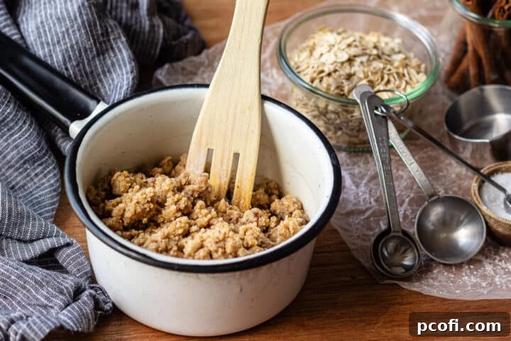 A bowl of streusel topping, garnished with oats and cinnamon, next to measuring spoons.