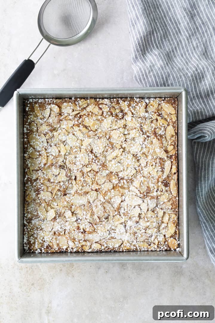 Cooled almond blondies dusted with powdered sugar, ready for slicing