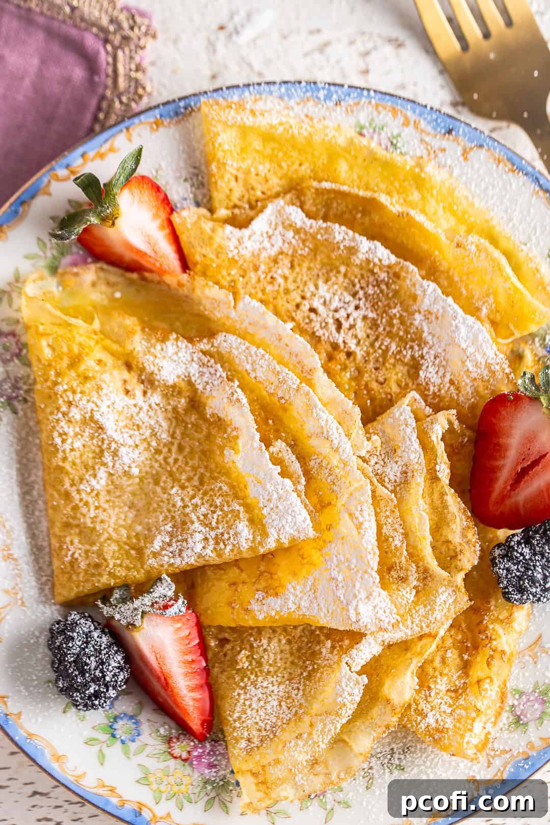 Easy crepe recipe, prepared and served on a vintage floral plate with powdered sugar and fresh berries.