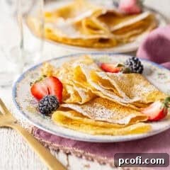 Freshly made crepe recipe presented on a vintage plate with fresh berries and powdered sugar.