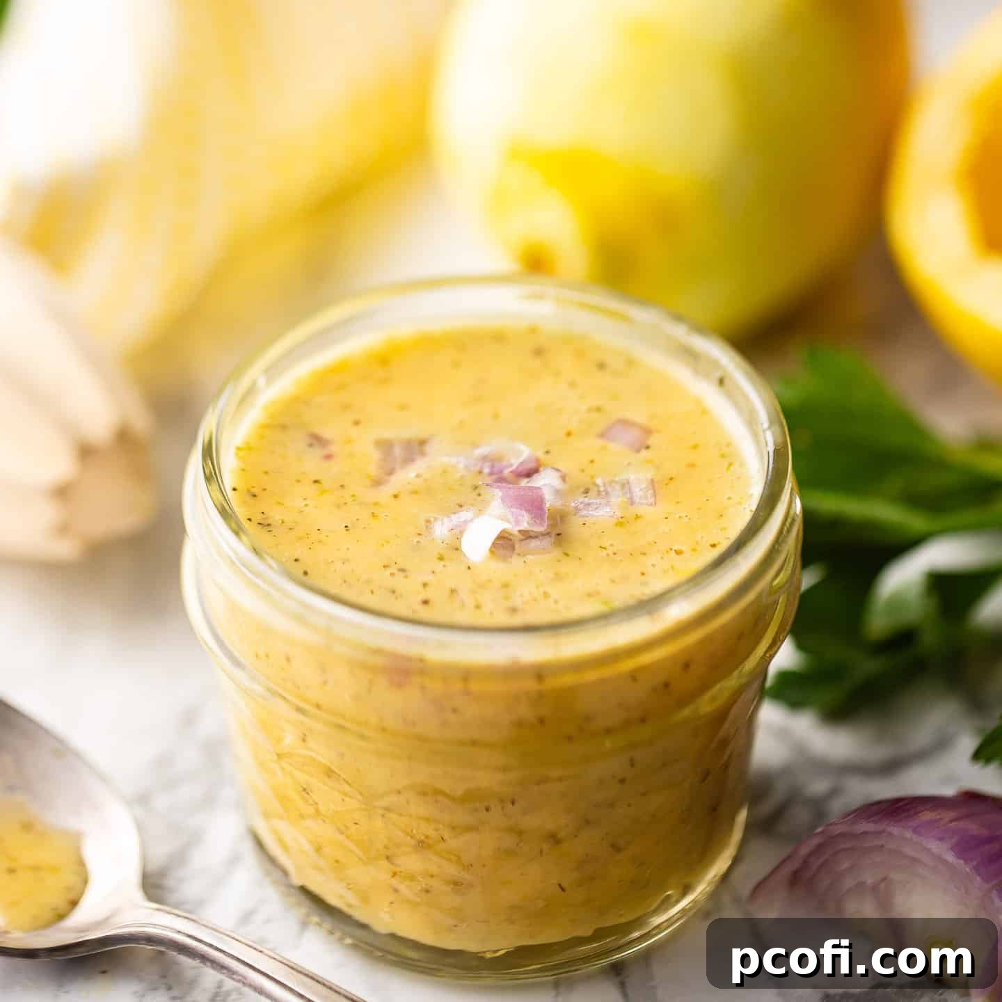 Homemade lemon vinaigrette, presented in a small glass jar and adorned with chopped shallots.