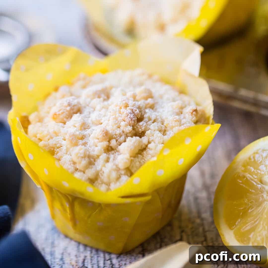Lemon crumb muffin in a yellow tulip cup with fresh lemon in the background.