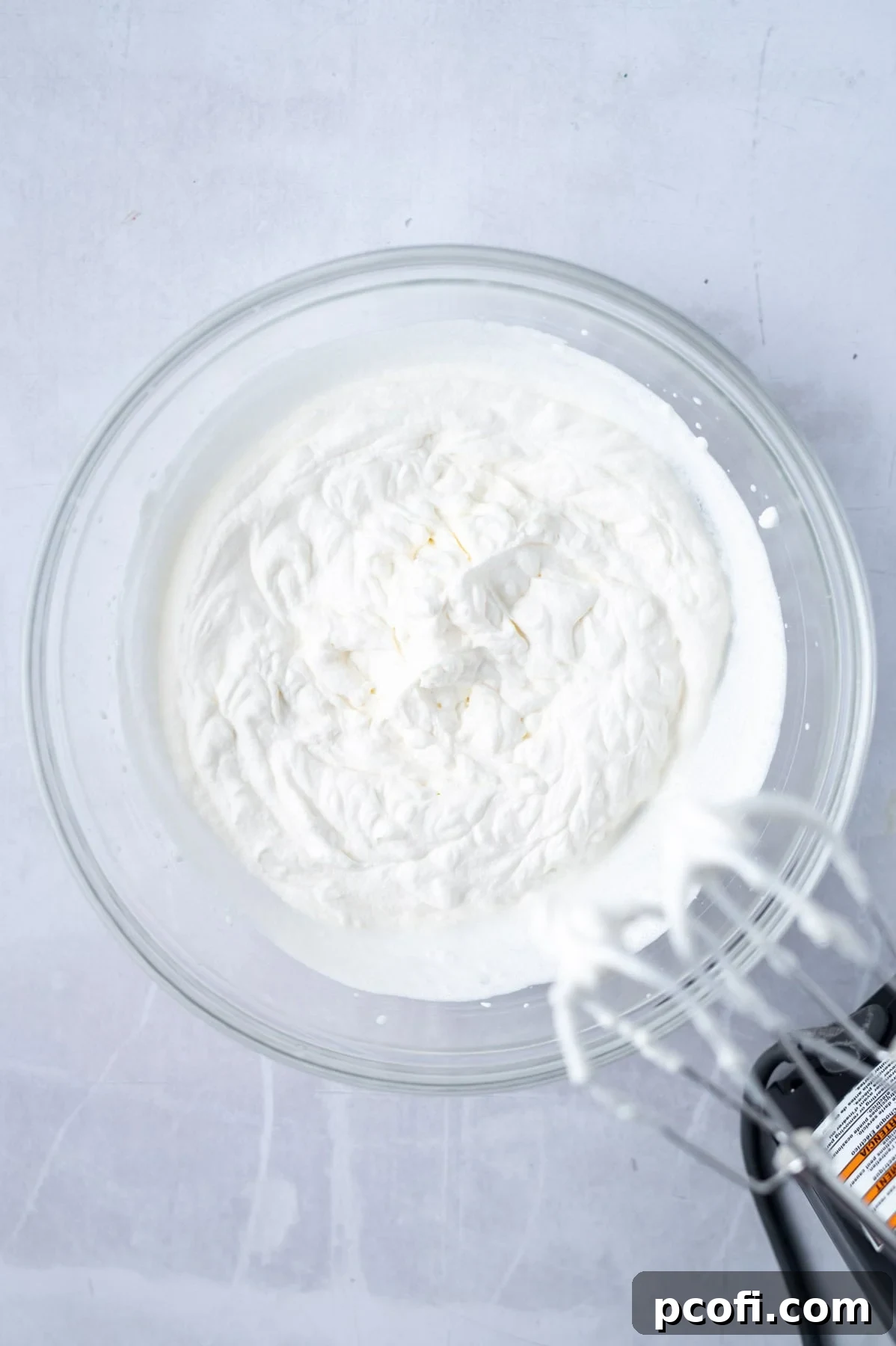 Homemade whipped cream being prepared in a mixing bowl with a hand mixer, achieving stiff peaks.