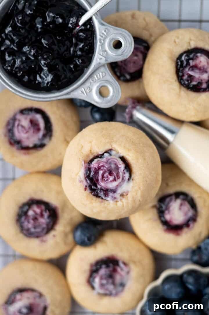 Blueberry and cream cookies cooling on a wire rack with a small measuring cup of blueberry jam in the background