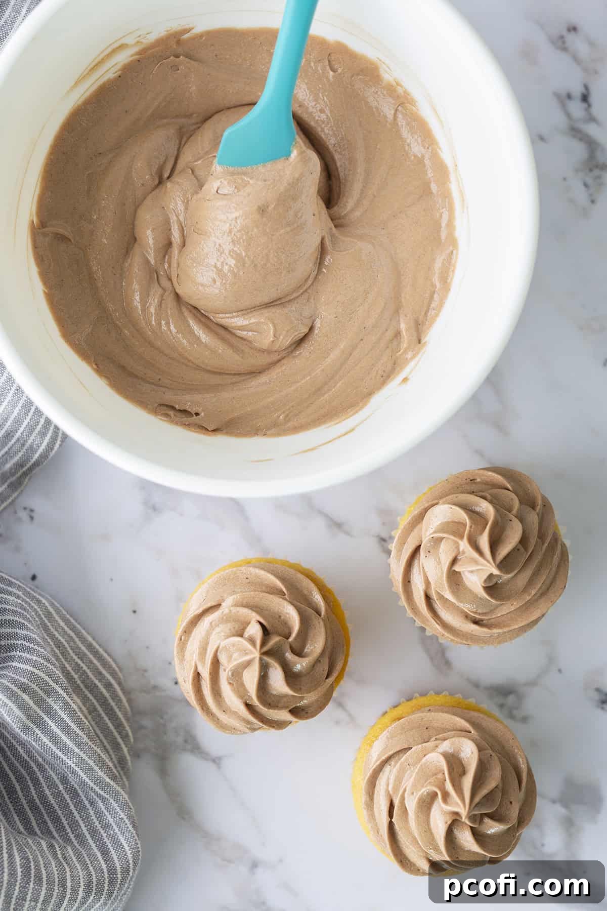 Decadent Chocolate Ermine Frosting in a bowl, alongside three perfectly frosted cupcakes, ready to be enjoyed.