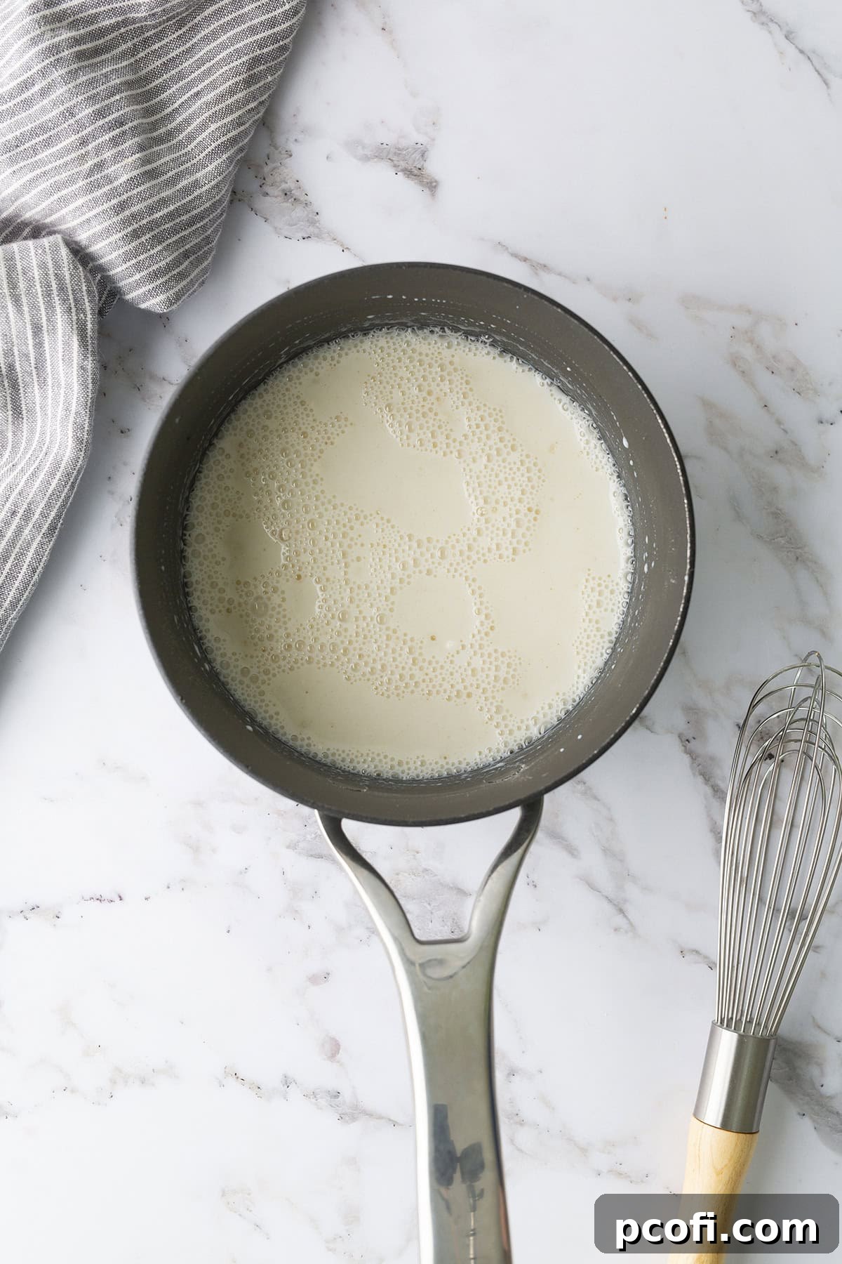 Whole milk being whisked into the dry flour and sugar mixture in a saucepan over heat.