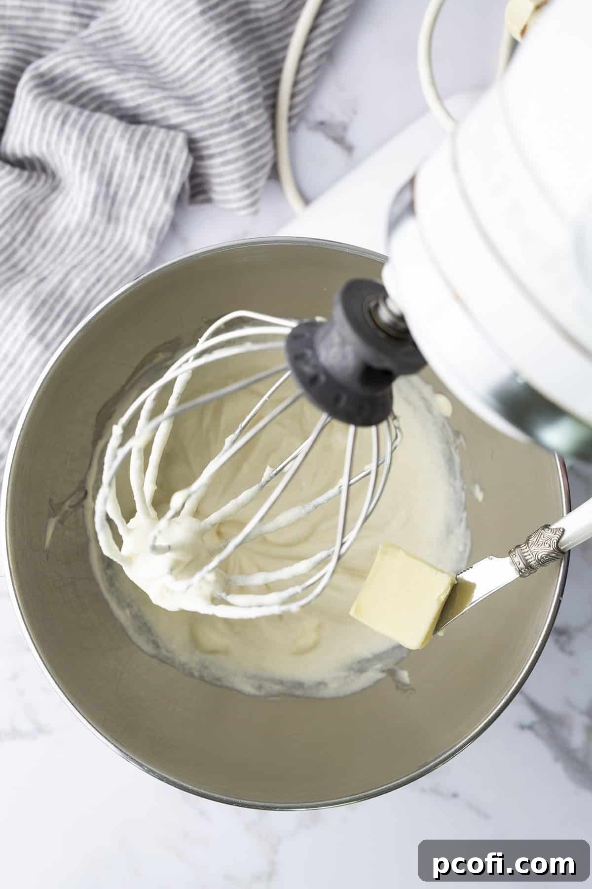 Softened butter being gradually added to the cooled ermine base in a stand mixer.