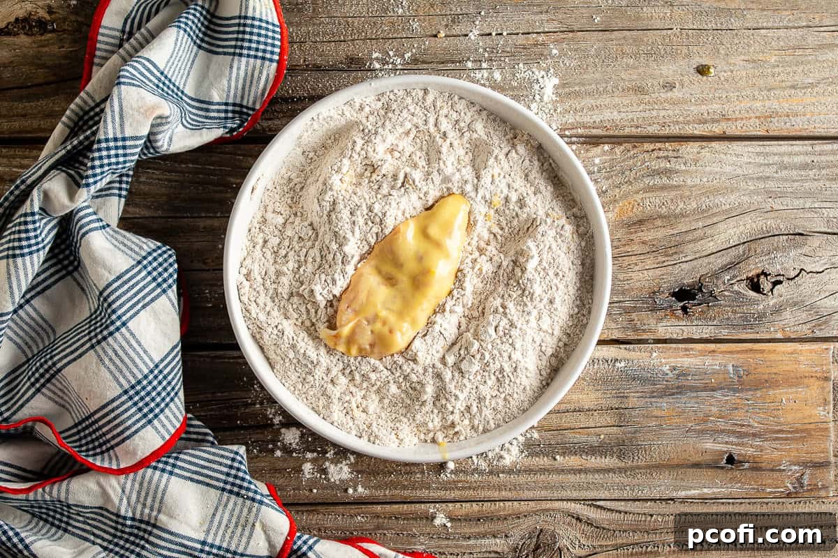 A batter-dipped chicken tender being thoroughly coated in the seasoned flour mixture for maximum crunch.