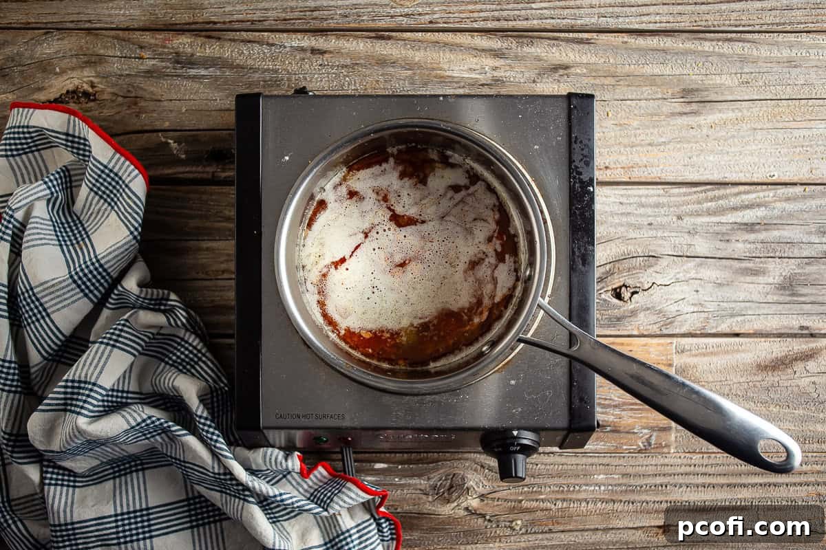 Honey and hot sauce being added to melted butter in a pot.
