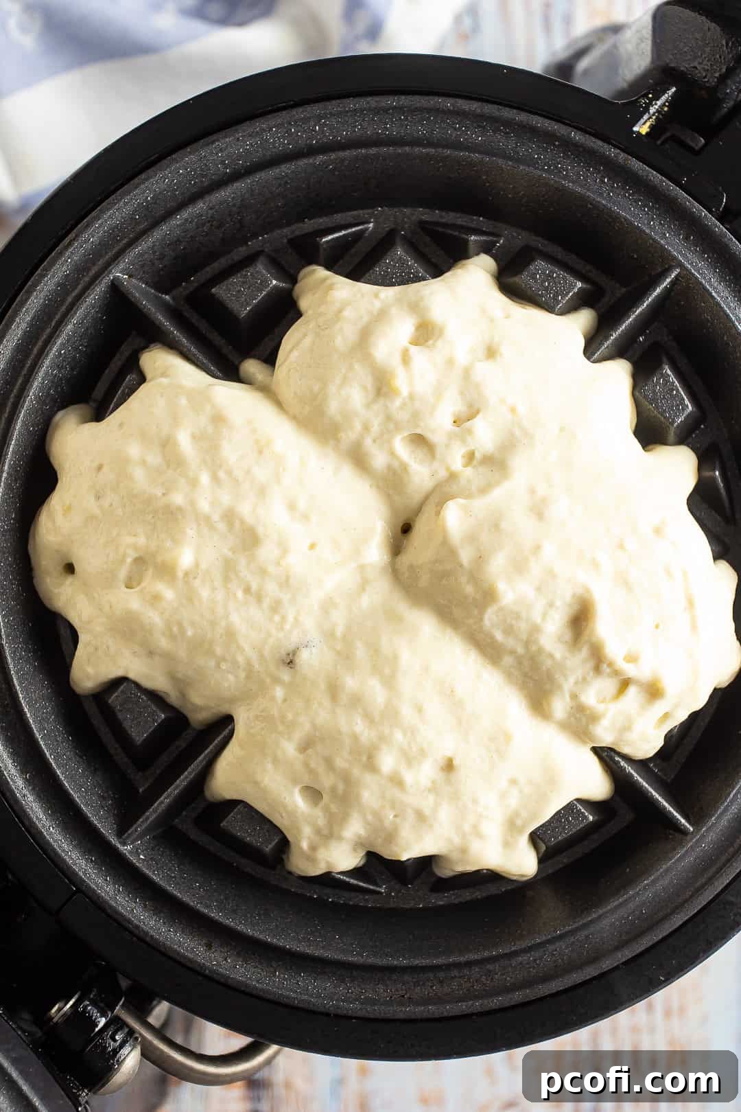 Freshly poured, uncooked waffle batter sitting on a hot waffle iron before closing.