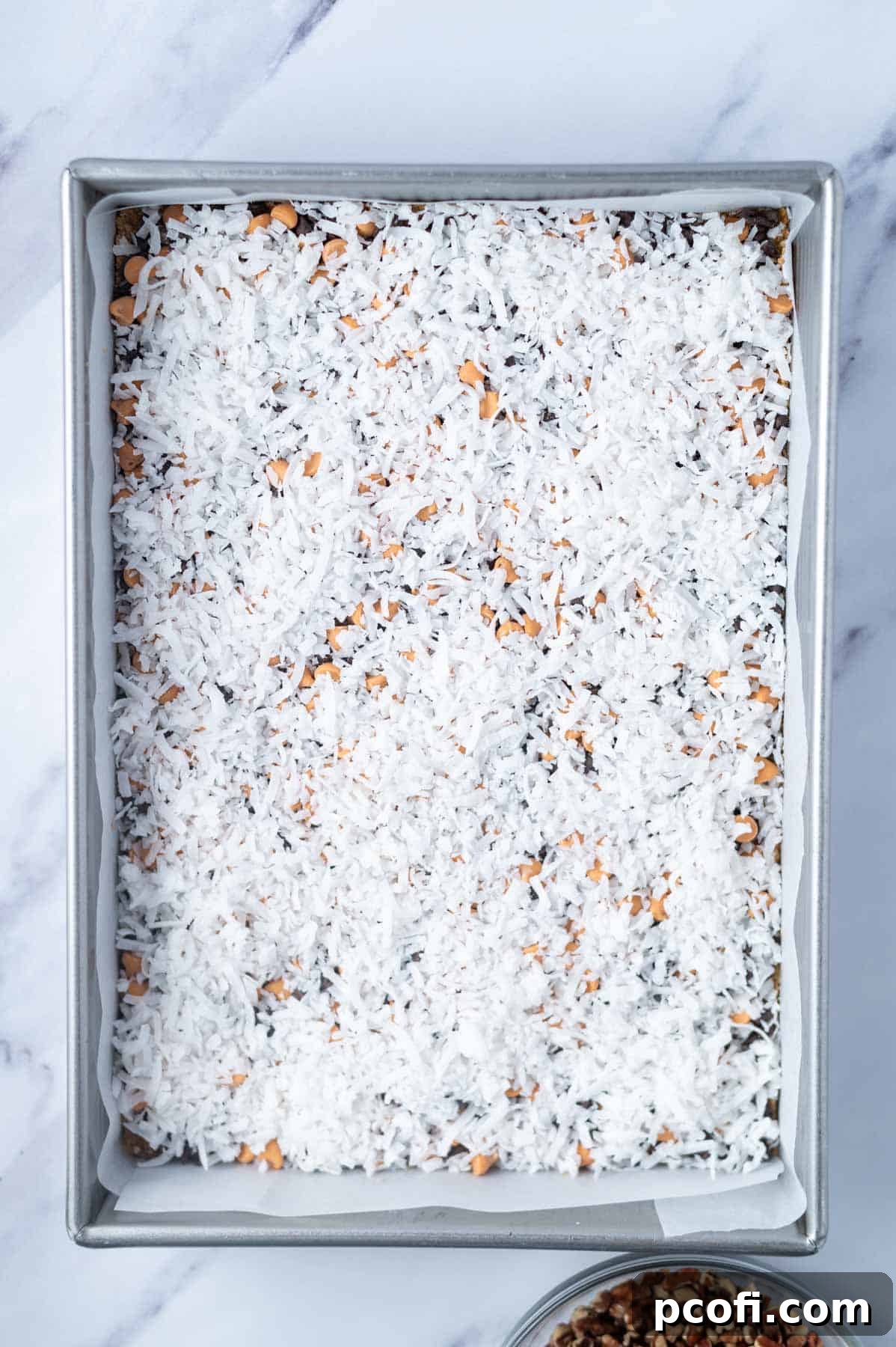 coconut layered over butterscotch and chocolate chips in a parchment lined baking pan