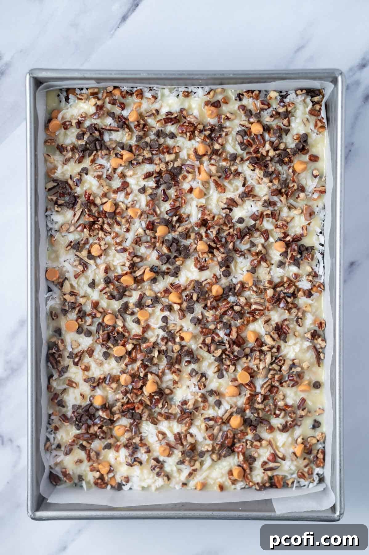 sweetened condensed milk poured over 7 layer bars in a parchment lined baking pan